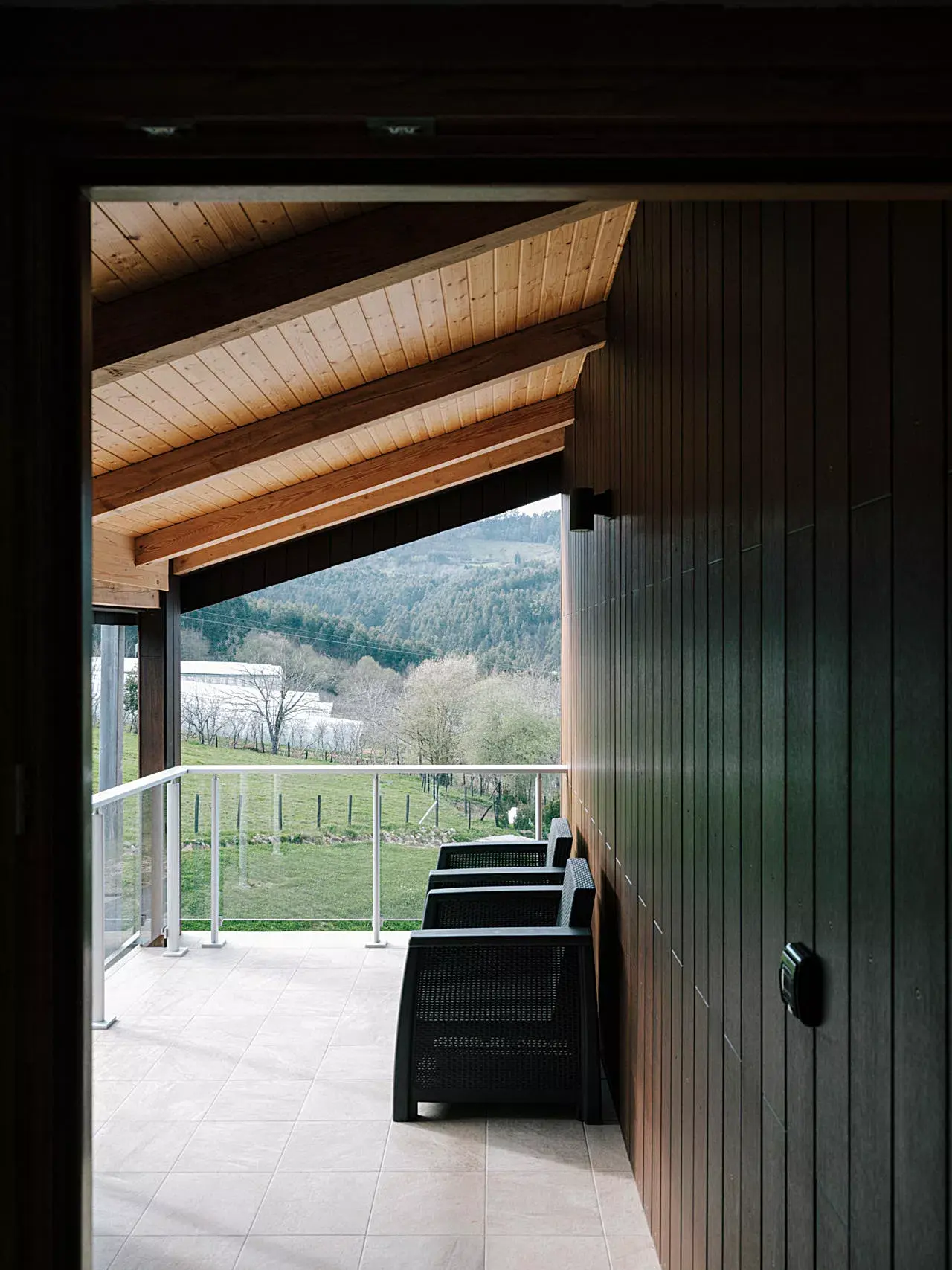 Vista desde el interior de una habitación hacia una terraza cubierta con suelo de baldosas, techo de madera