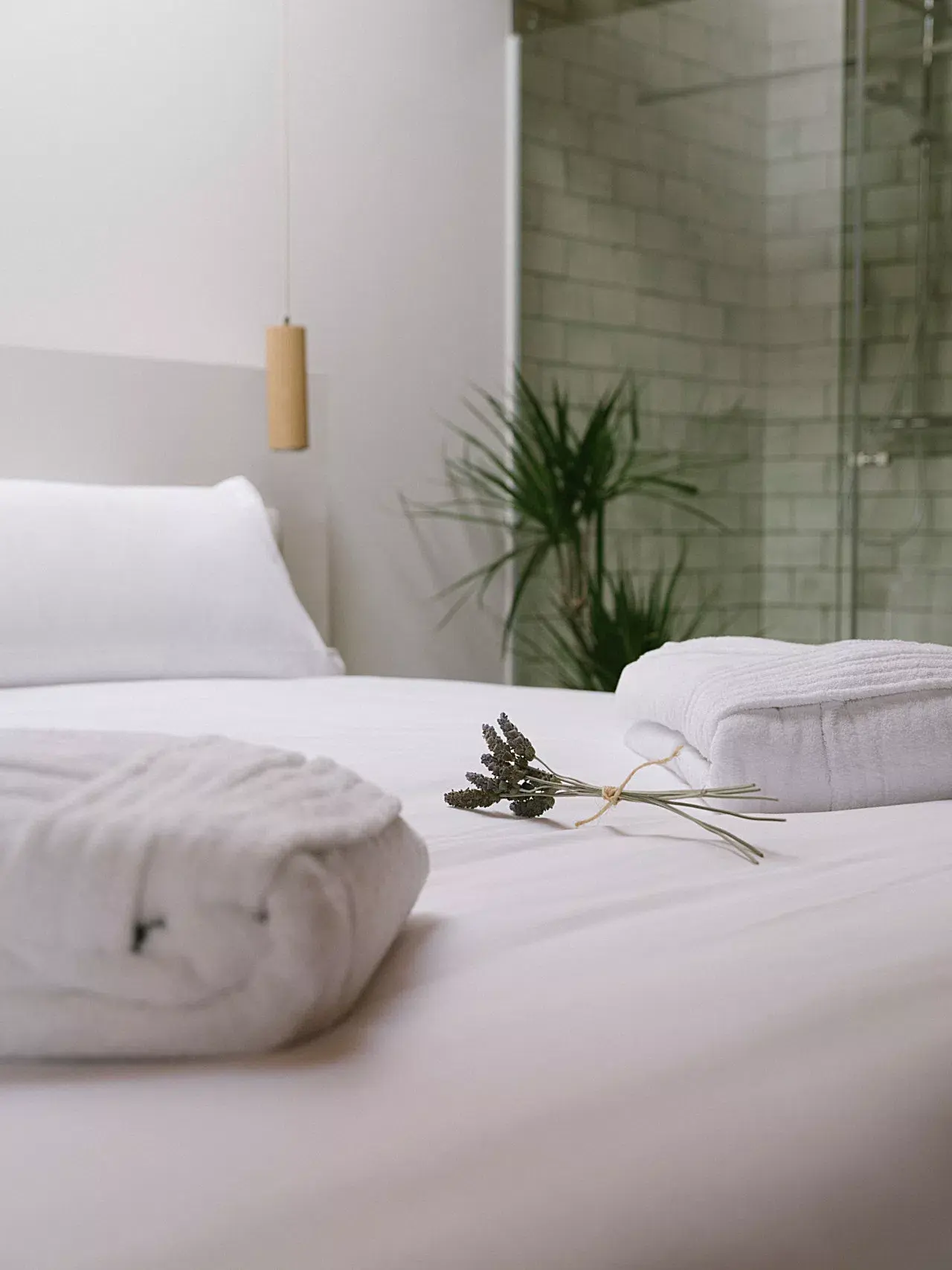 Vista de una habitación de hotel con una cama grande vestida de blanco, toallas enrolladas y un ramo de lavanda