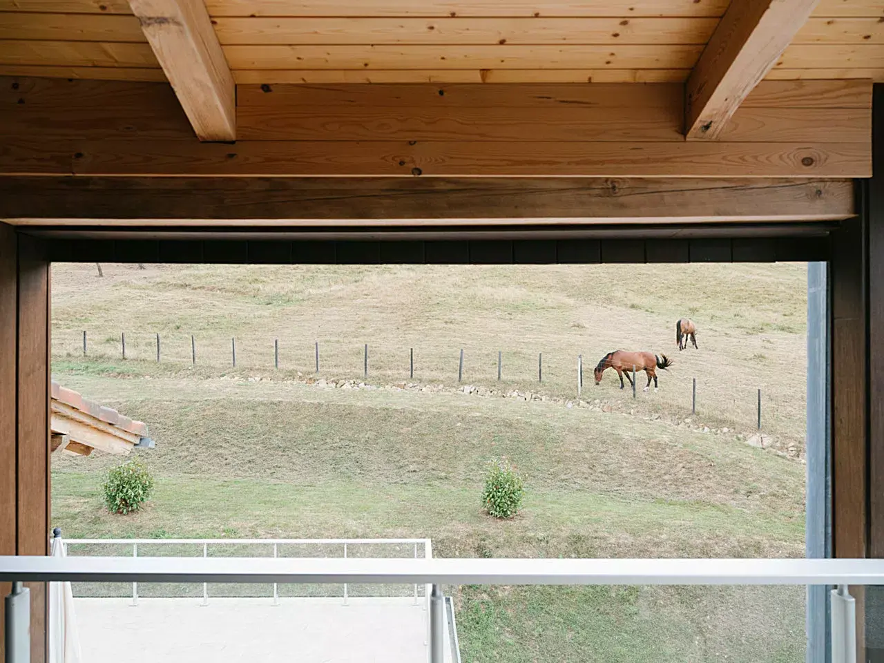Vista desde el interior de una habitación a través de una ventana abierta con marco de madera y techo de vigas vistas.