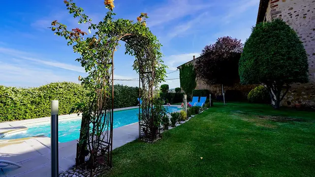 Vista exterior de una piscina rectangular con agua azul rodeada de césped verde, un arco de rosales trepadores, setos