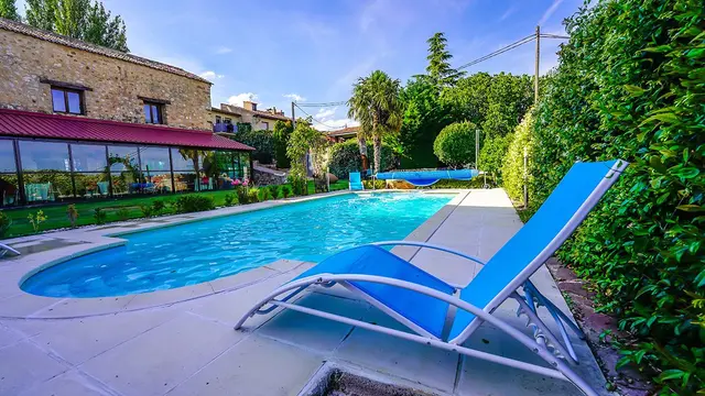Vista exterior de una piscina rectangular con agua azul clara, rodeada de un solárium de piedra.
