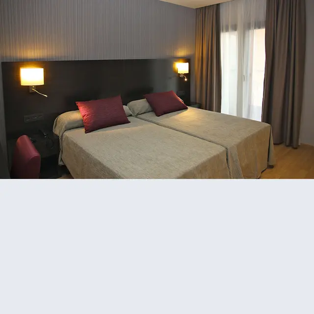 Habitación de hotel con dos camas individuales, cabecero oscuro, lámparas de pared y cortinas junto a la ventana.