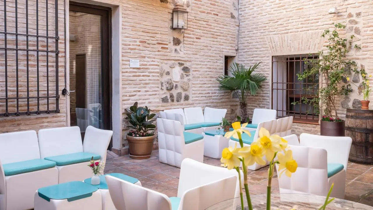 Patio exterior de un edificio con paredes de ladrillo visto, amueblado con sofás y sillones blancos con cojines
