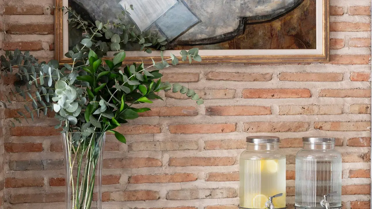 Decoración en una habitación con pared de ladrillo visto, un jarrón alto con ramas de eucalipto, dos dispensadores