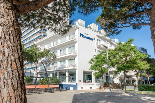 Vista exterior del Hotel Planamar, un edificio blanco de varias plantas con balcones, rodeado de árboles y bajo