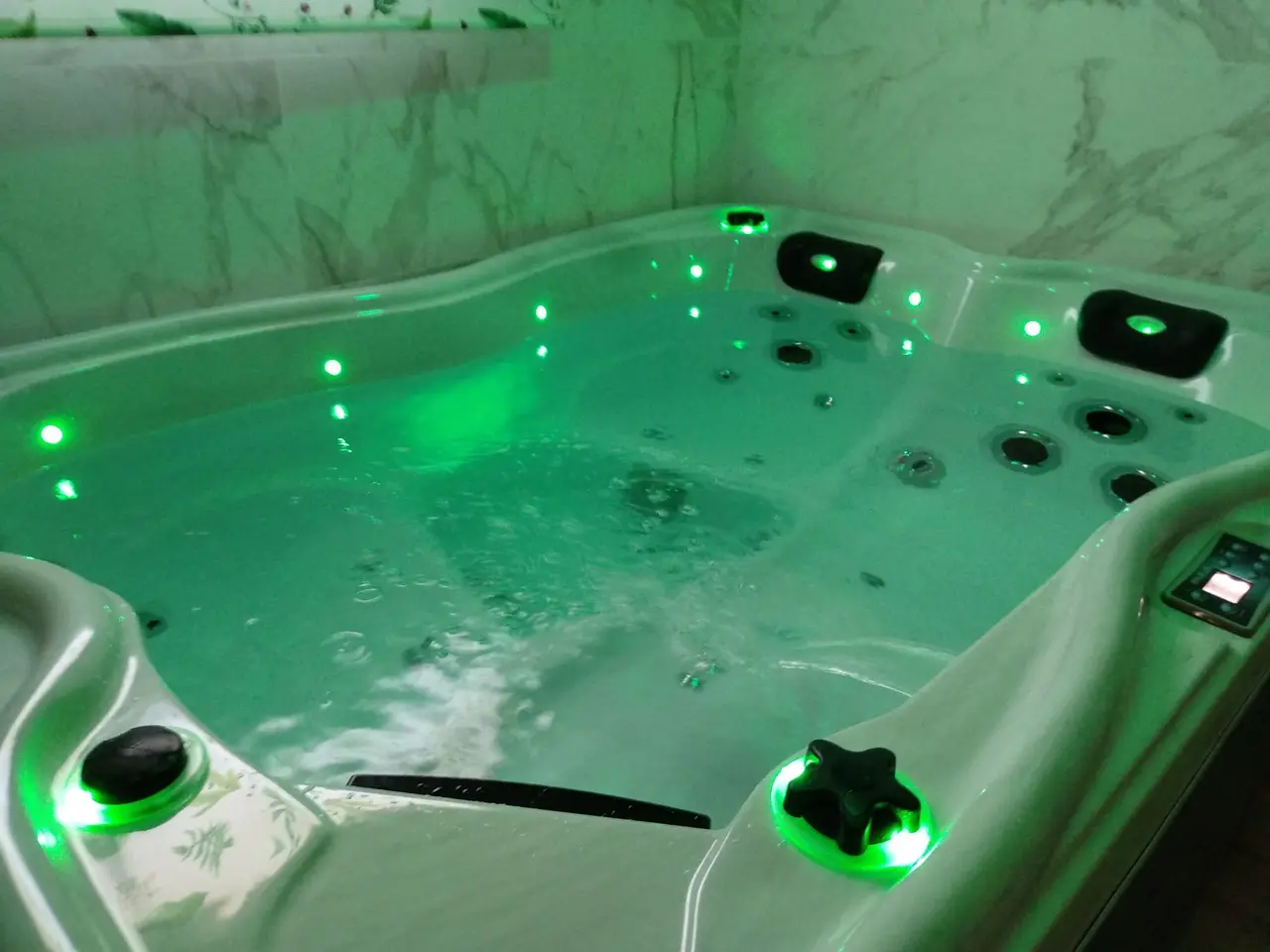 Jacuzzi de hidromasaje con agua iluminada en verde, múltiples jets y asientos, instalado en una habitación con paredes