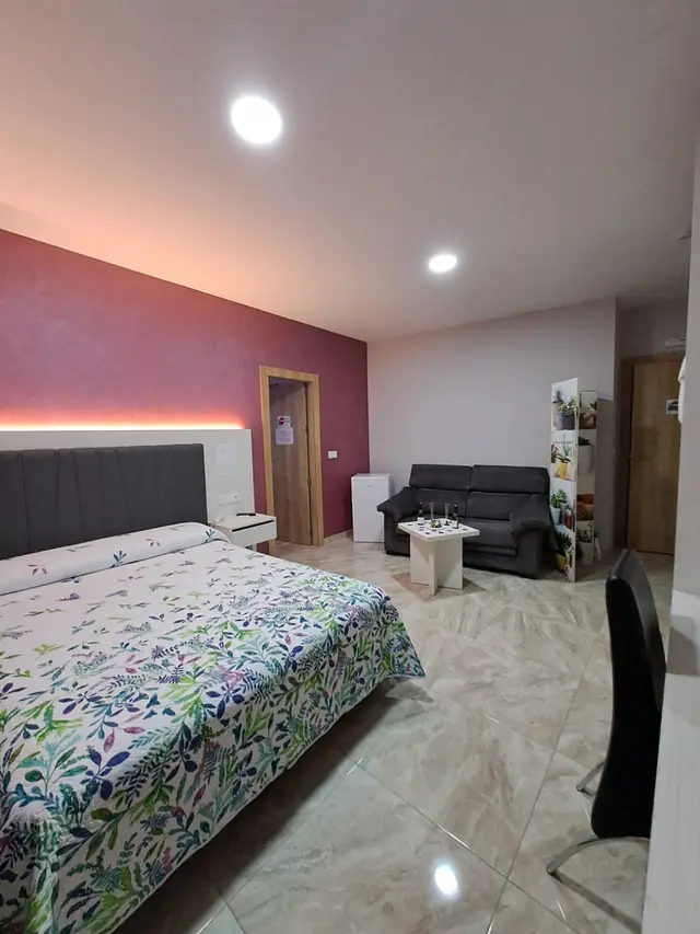 Habitación de hotel con cama grande cubierta por edredón de estampado floral, cabecero gris, pared roja