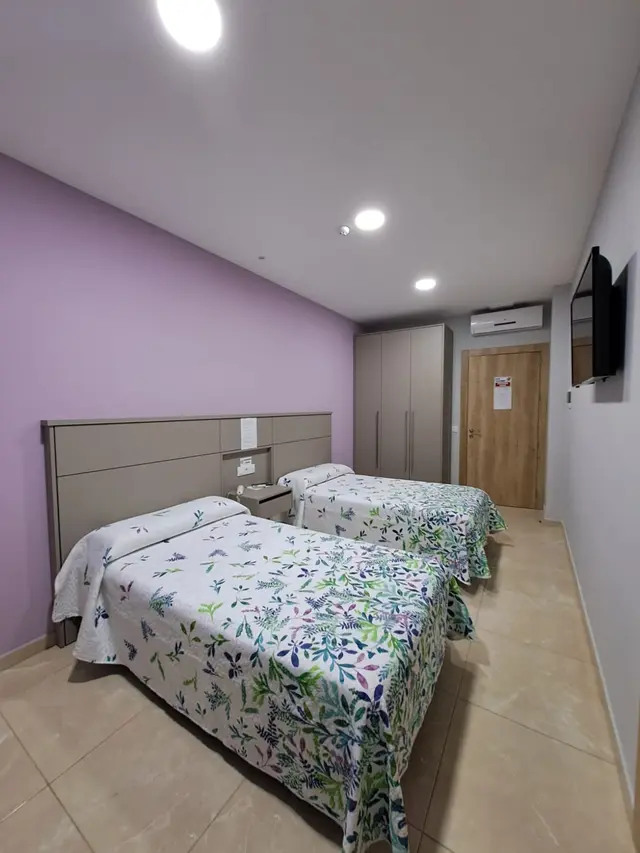 Habitación de hotel con dos camas individuales cubiertas con colchas de estampado floral en tonos verdes y morados