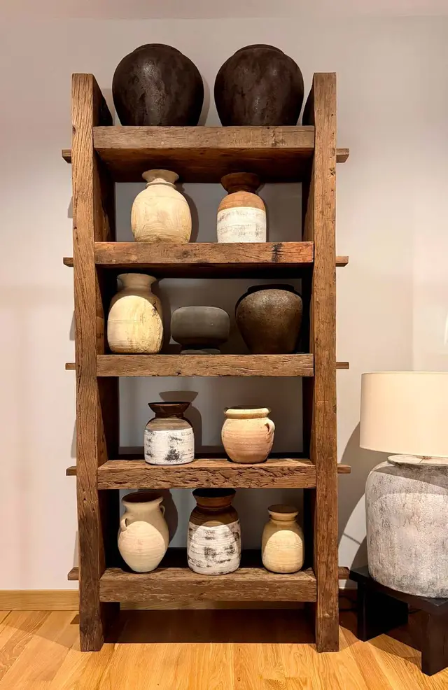 Estantería de madera rústica con varios jarrones y vasijas de cerámica antigua de diferentes tamaños y tonos, colocada