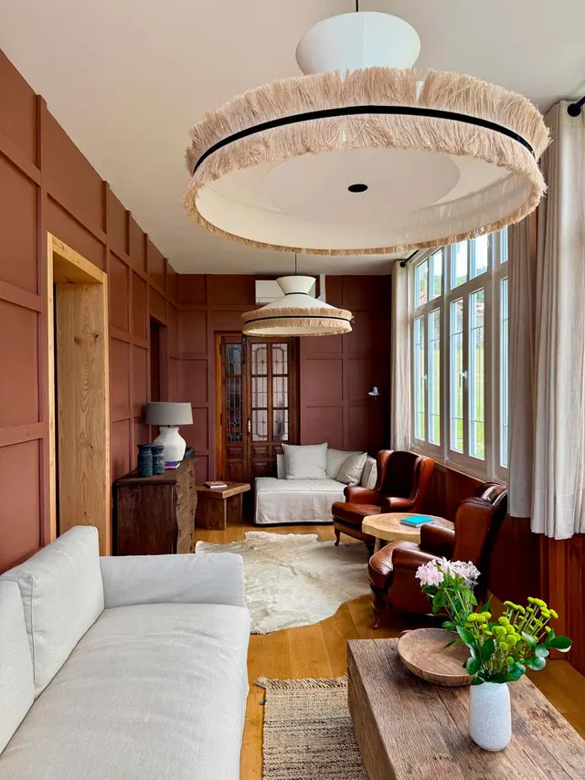 Interior de una sala de estar con paredes en tonos terracota y paneles de madera, suelo de parquet, un sofá blanco