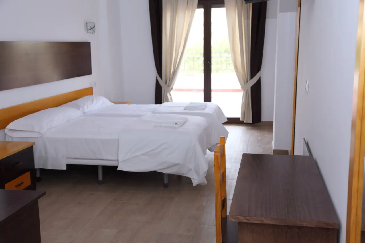 Habitación de hotel con dos camas individuales vestidas con sábanas blancas, cabecero de madera y panel decorativo