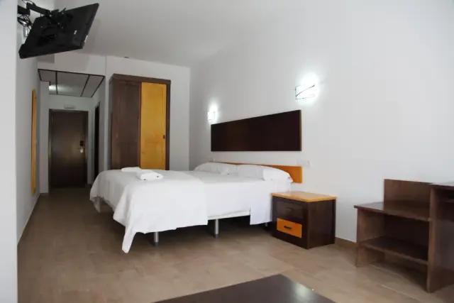 Habitación de hotel con dos camas individuales cubiertas con colchas blancas, cabecero oscuro en la pared, mesita