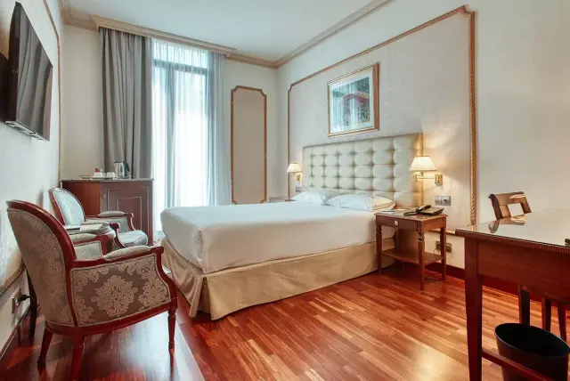 Habitación de hotel con cama doble grande, cabecero acolchado, escritorio de madera, sillón tapizado, televisor en la pa
