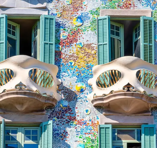 Fachada exterior de un edificio modernista con mosaicos de colores, balcones en forma de calavera y ventanas