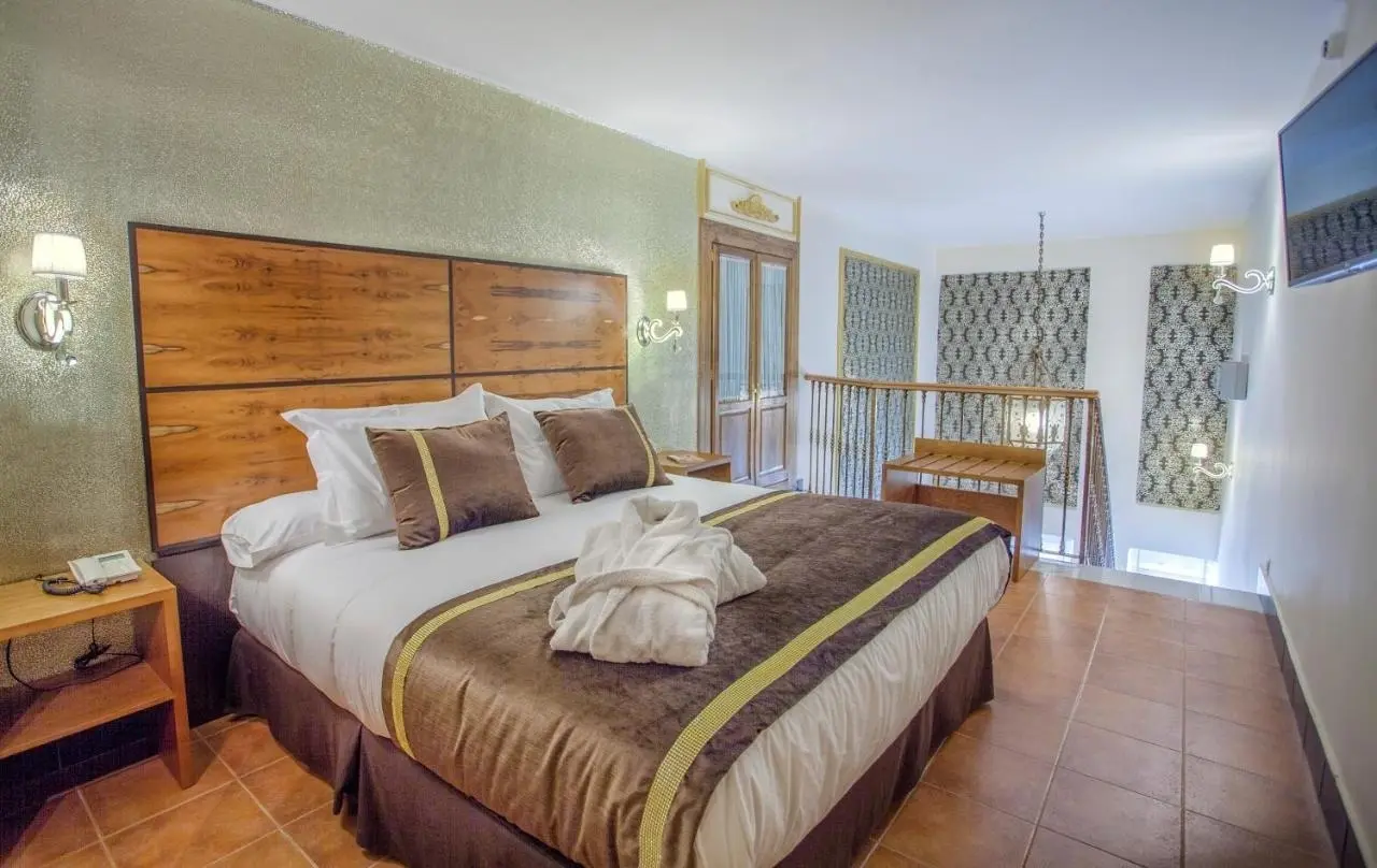 Vista de una junior suite con cama king size vestida con sábanas blancas, cojines marrones y una toalla doblada