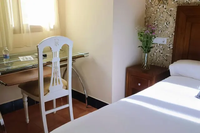 Vista de una habitación de hotel con una cama de matrimonio con sábanas blancas, mesita de noche de madera, escritorio