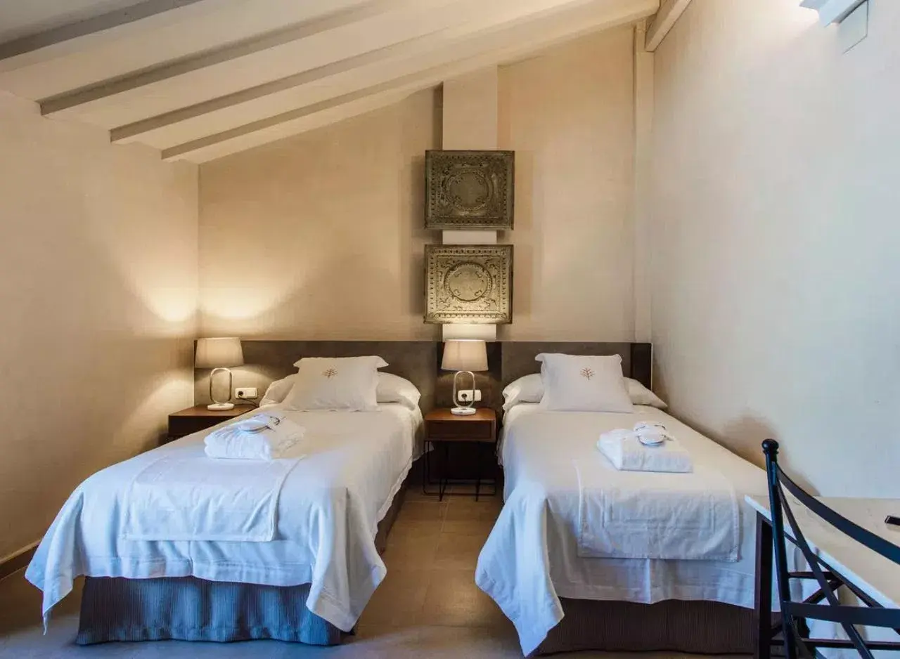 Habitación con dos camas individuales vestidas con sábanas blancas, almohadas y toallas enrolladas.