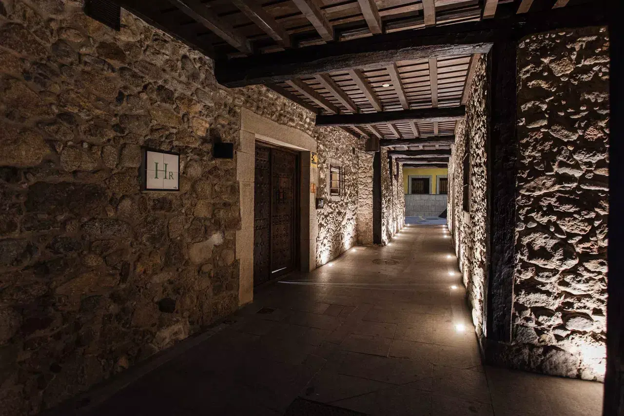 Pasillo interior de un spa con paredes de piedra rústica, techo de vigas de madera, iluminación cálida en el suelo