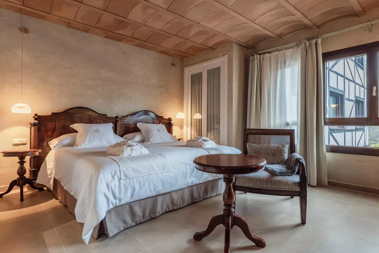 Habitación con cama doble de madera oscura, dosel de madera en el techo, mesita redonda de centro, sillón