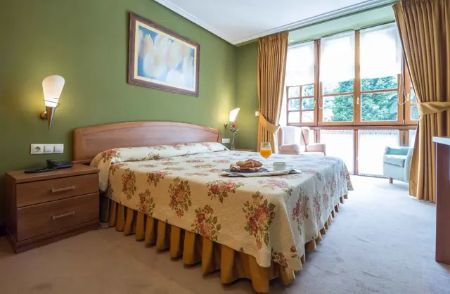 Habitación de hotel con cama doble, mesitas de noche, ventanal con cortinas y vista al exterior.