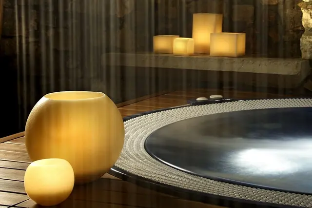 Vista de un jacuzzi circular con agua iluminada, rodeado de una plataforma de madera y piedras.