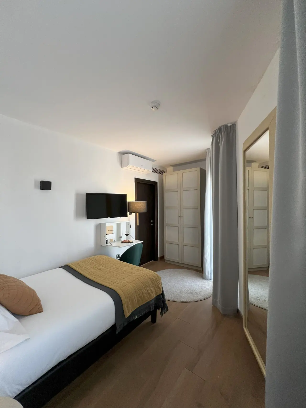 Vista de una habitación de hotel con cama doble con colcha amarilla, escritorio con silla verde, televisor