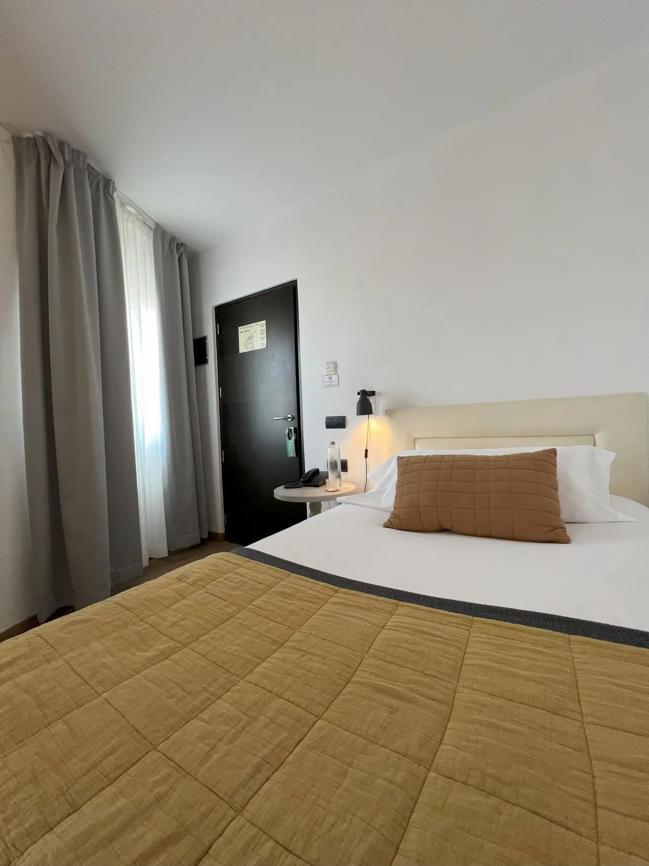 Habitación de hotel con cama doble grande cubierta por edredón amarillo acolchado y cojines blancos y marrones, mesita