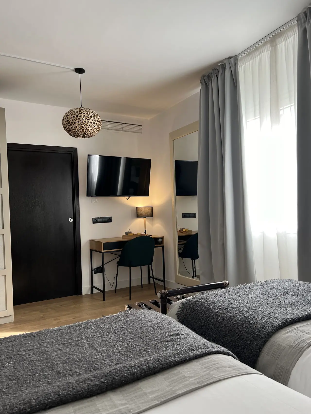 Habitación de hotel con dos camas individuales cubiertas por colchas grises, escritorio de madera con silla verde