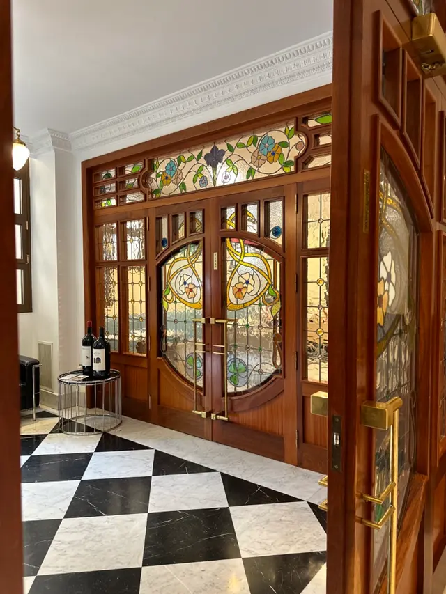 Entrada a una sala con puertas de madera y cristaleras de estilo modernista con vidrieras de colores, suelo de damero