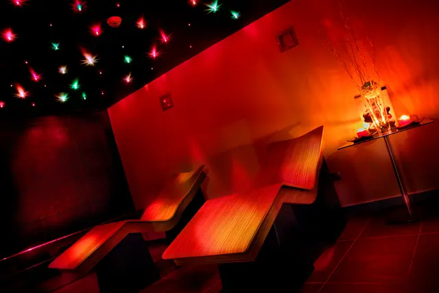 Interior de un spa privado con dos tumbonas de madera iluminadas en rojo, techo negro con luces de colores simulando