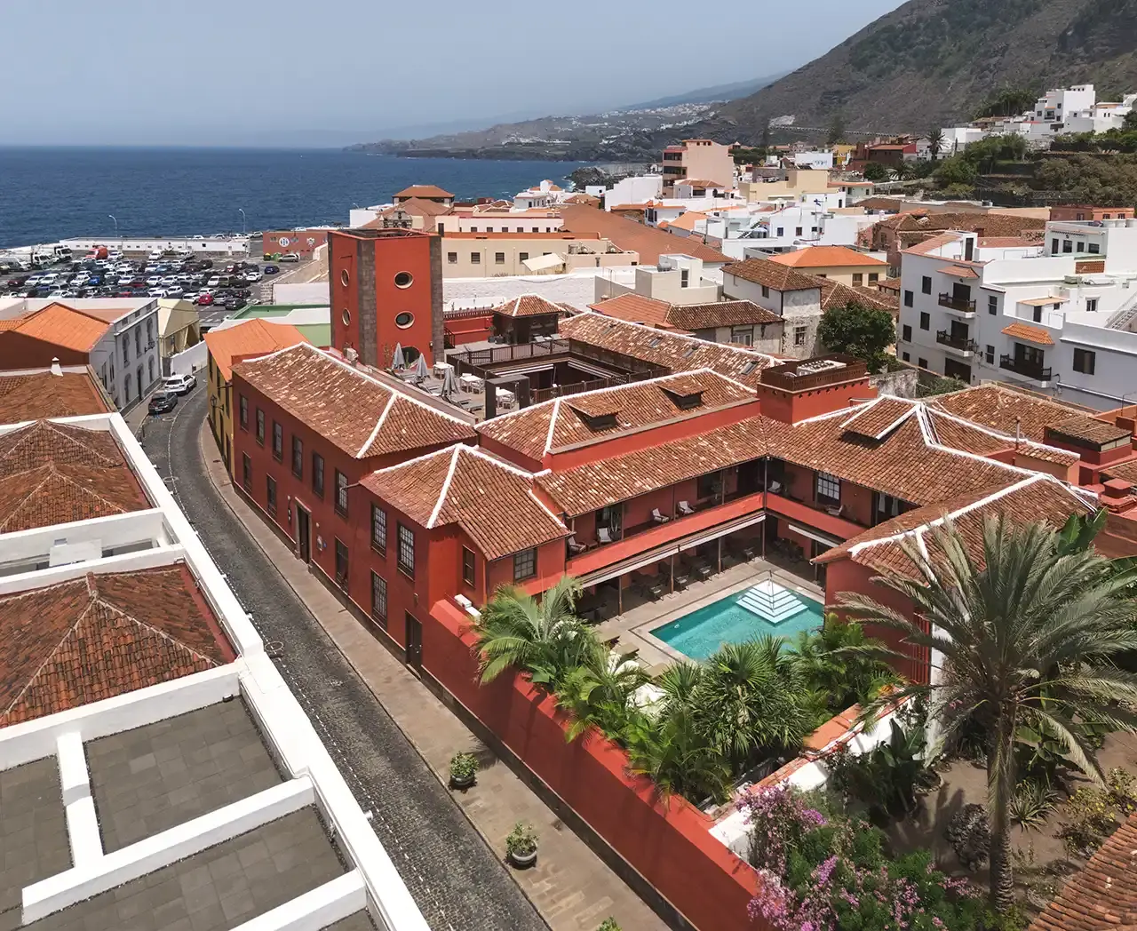 Vista aérea del hotel con patio interior que incluye una piscina rectangular rodeada de vegetación, edificios