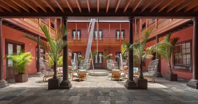Patio interior de un hotel con suelo de piedra, columnas de madera, techo con vigas, varias sillas y sillones