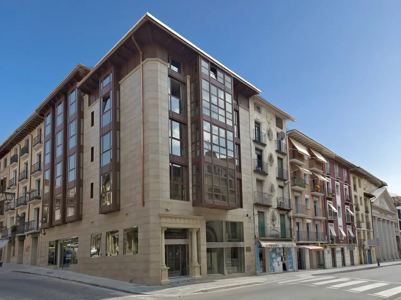 Fachada exterior de un edificio de hotel de varias plantas con fachada de piedra clara y ventanas de madera oscura
