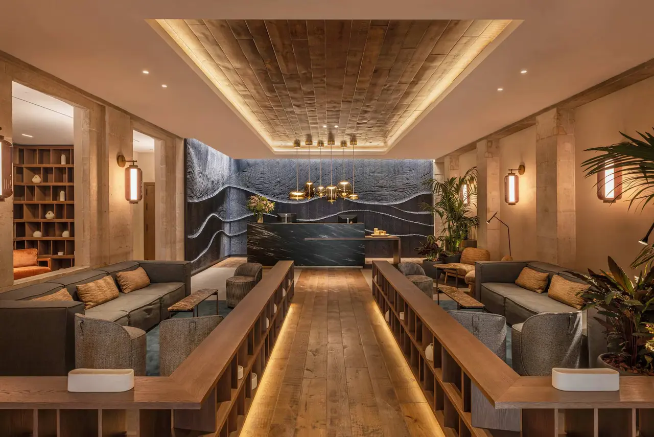 Interior de un spa con paredes de piedra, techo de madera, iluminación cálida y zona de espera con sofás grises