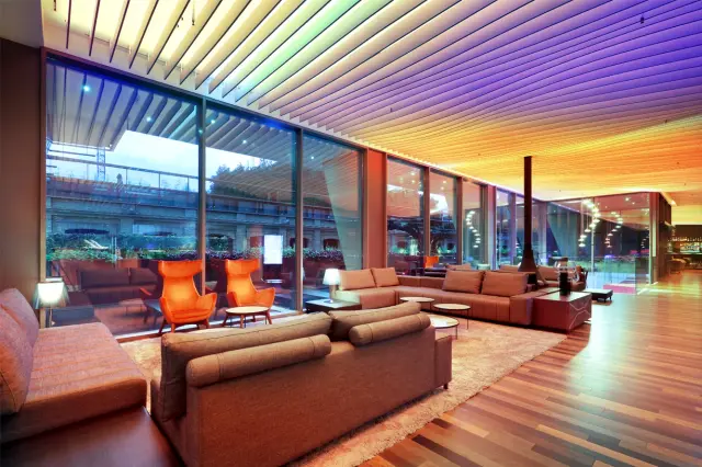 Interior de una suite de hotel con zona de estar amueblada con sofás y sillones de color tierra, grandes ventanales que 