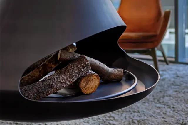 Detalle de una chimenea moderna de diseño curvo en color negro, con leña apilada en su interior, sobre una alfombra