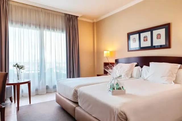 Habitación de hotel con dos camas grandes separadas, ropa de cama blanca, cabecero de madera oscura y tres cuadros