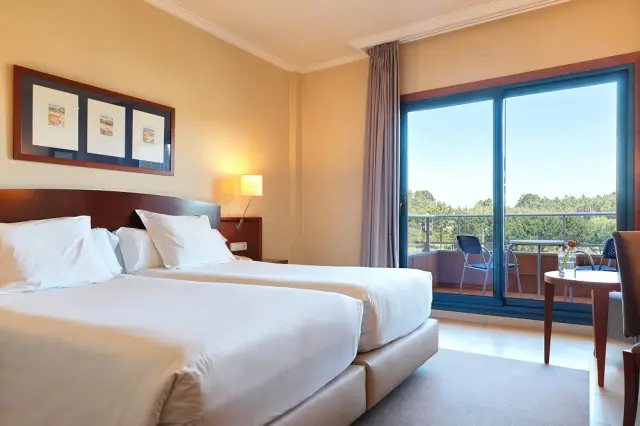 Habitación de hotel con dos camas grandes vestidas de blanco, cabecero de madera oscura, tres cuadros enmarcados