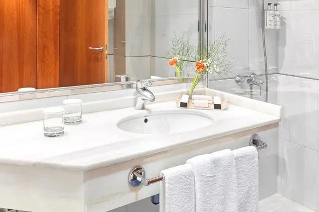 Detalle del lavabo de mármol blanco con grifo cromado, dos vasos de cristal, toallas blancas colgadas en un toallero