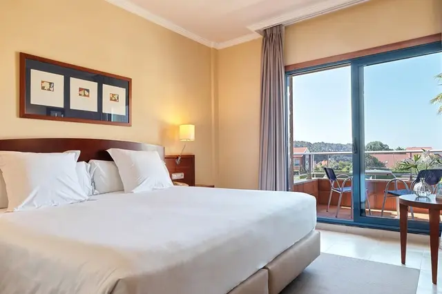 Habitación de hotel con cama grande vestida de blanco, cabecero de madera, tres cuadros en la pared, mesita de noche