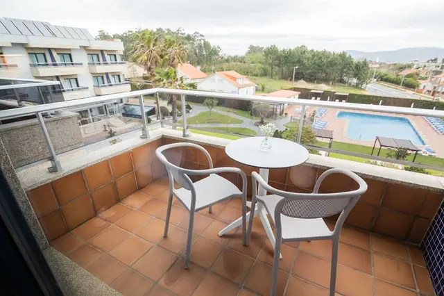 Vista desde el balcón de la habitación con mesa y sillas, mostrando una piscina exterior, edificios y paisaje al fondo.