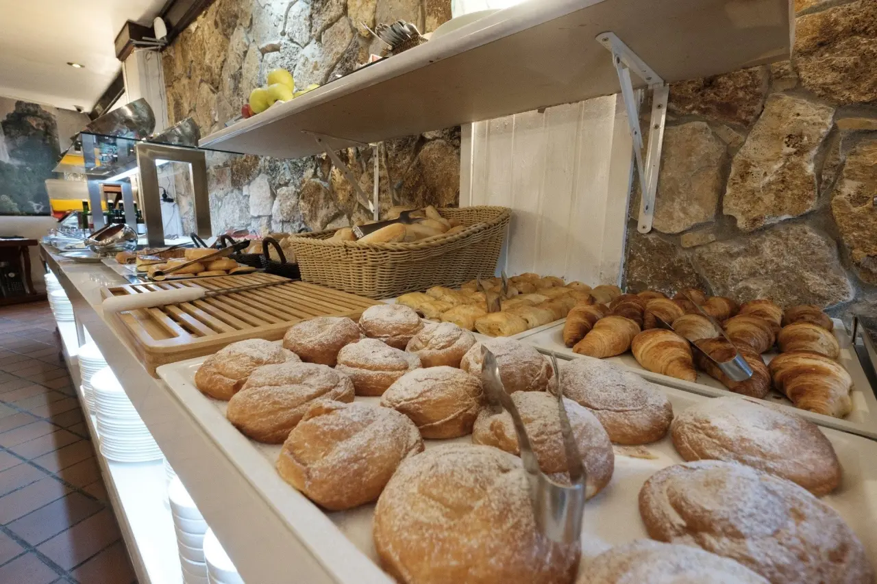 Mostrador de desayuno con variedad de bollería, cruasanes y pasteles sobre una mesa junto a una pared de piedra.