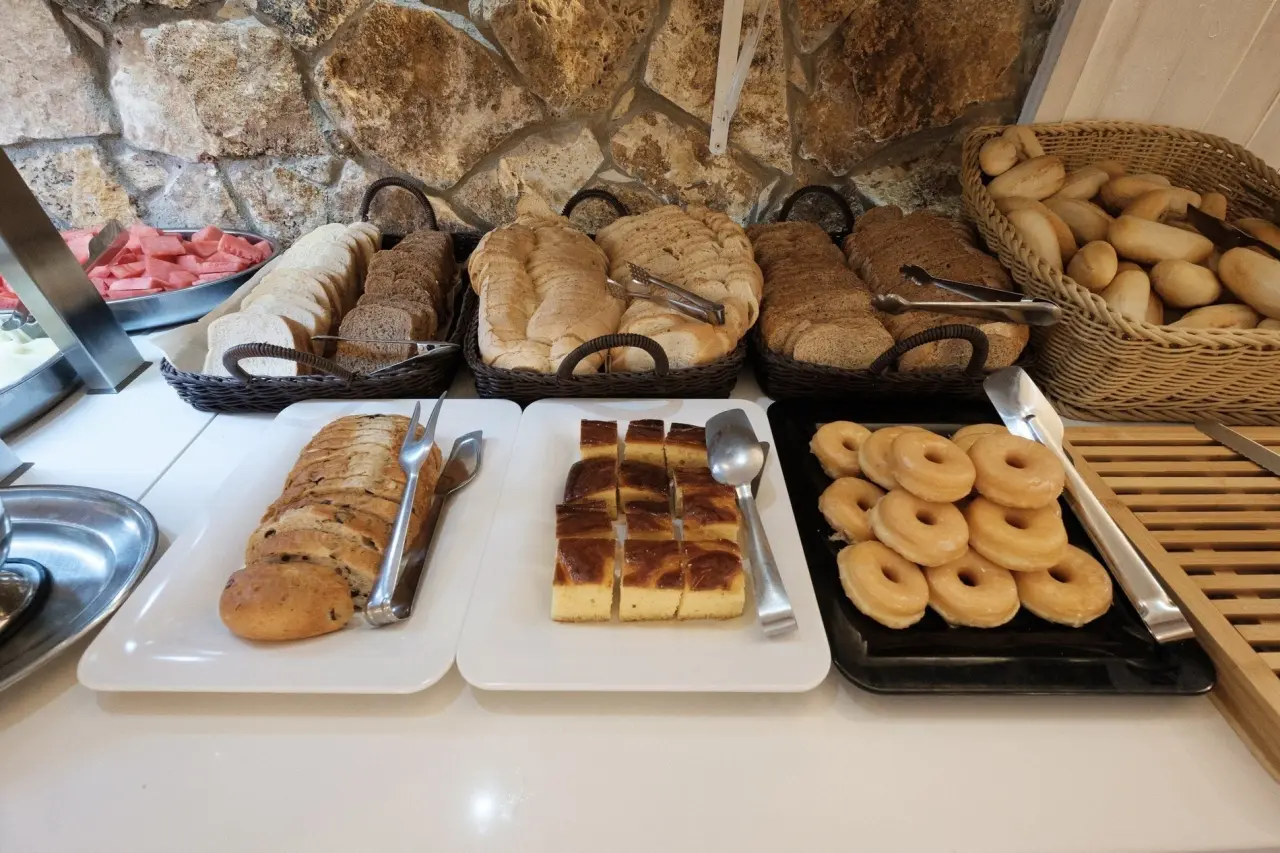 Mesa de desayuno con cestas de panes variados, donuts glaseados, trozos de bizcocho y sandía en un buffet