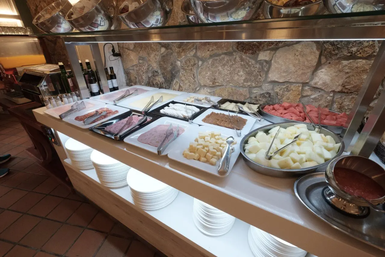 Buffet de desayuno con quesos, embutidos, frutas y salsas en mostrador de autoservicio.