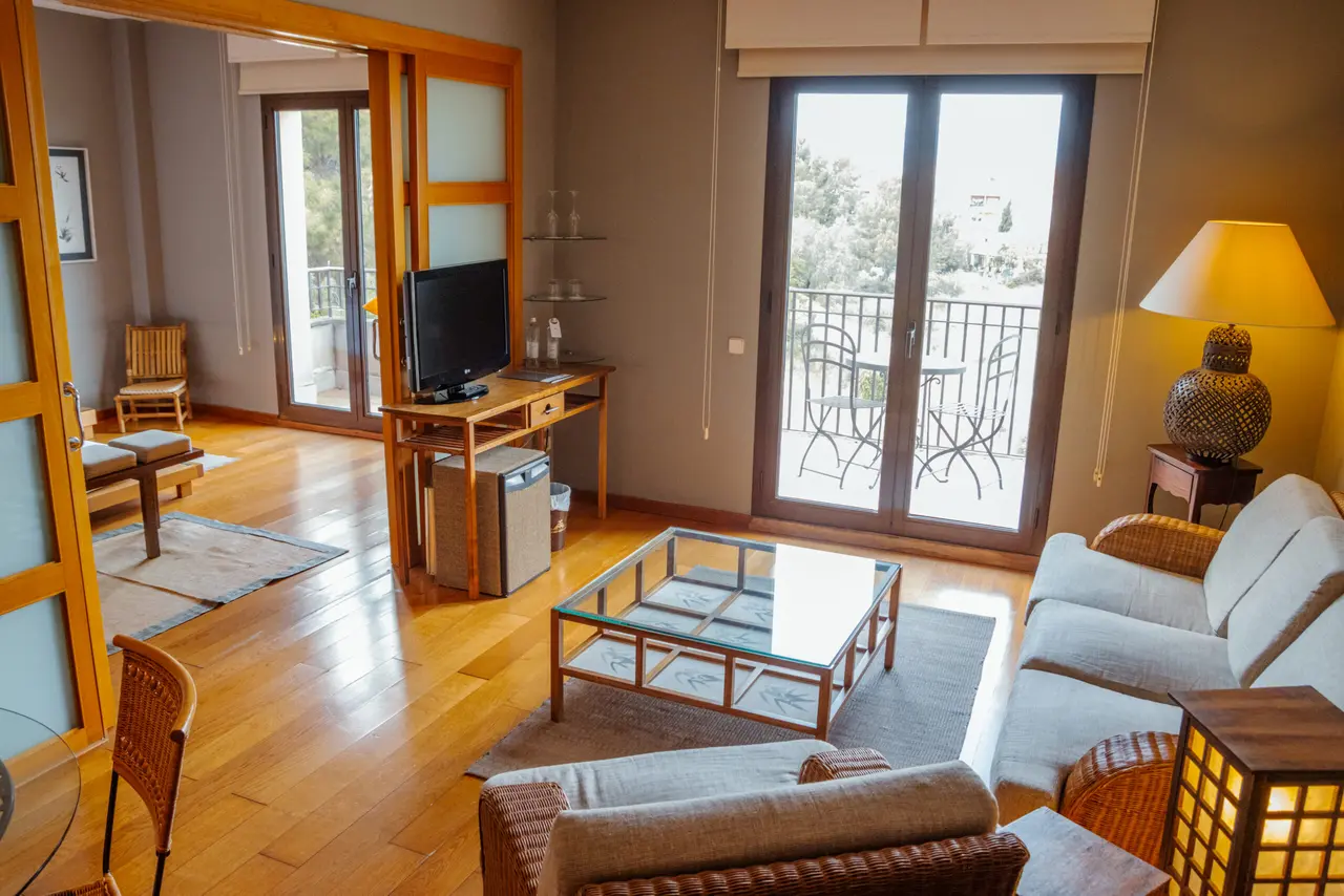 Vista de una suite con suelo de madera clara, sofá de mimbre, mesa de centro de cristal, televisor sobre un mueble