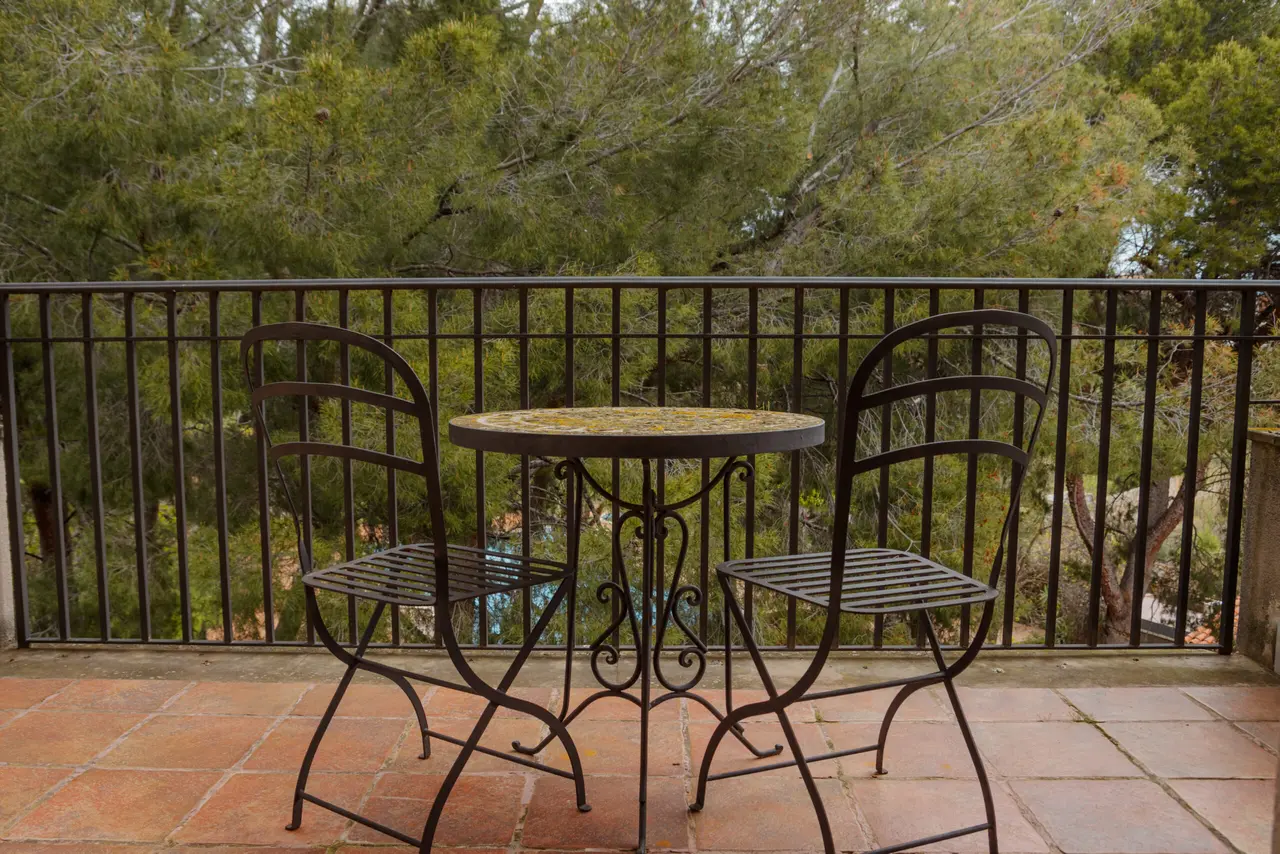 Terraza privada con mesa y dos sillas de forja sobre suelo de terracotta, barandilla metálica y vistas a un bosque