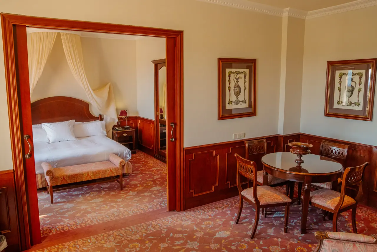 Vista de una suite de hotel con una zona de estar que incluye una mesa redonda de madera con cuatro sillas tapizadas