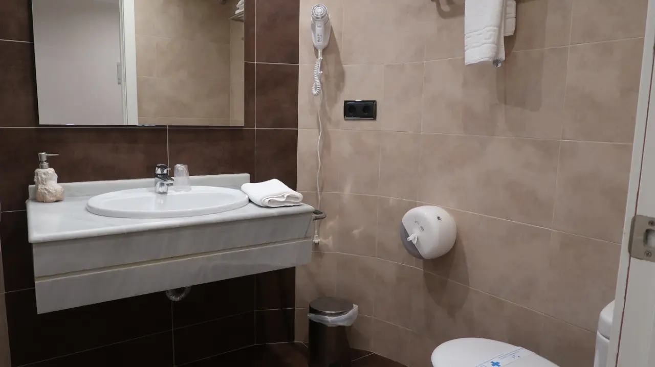 Baño de la Junior Suite con lavabo sobre encimera de mármol, espejo grande, secador de pelo en la pared, dispensador