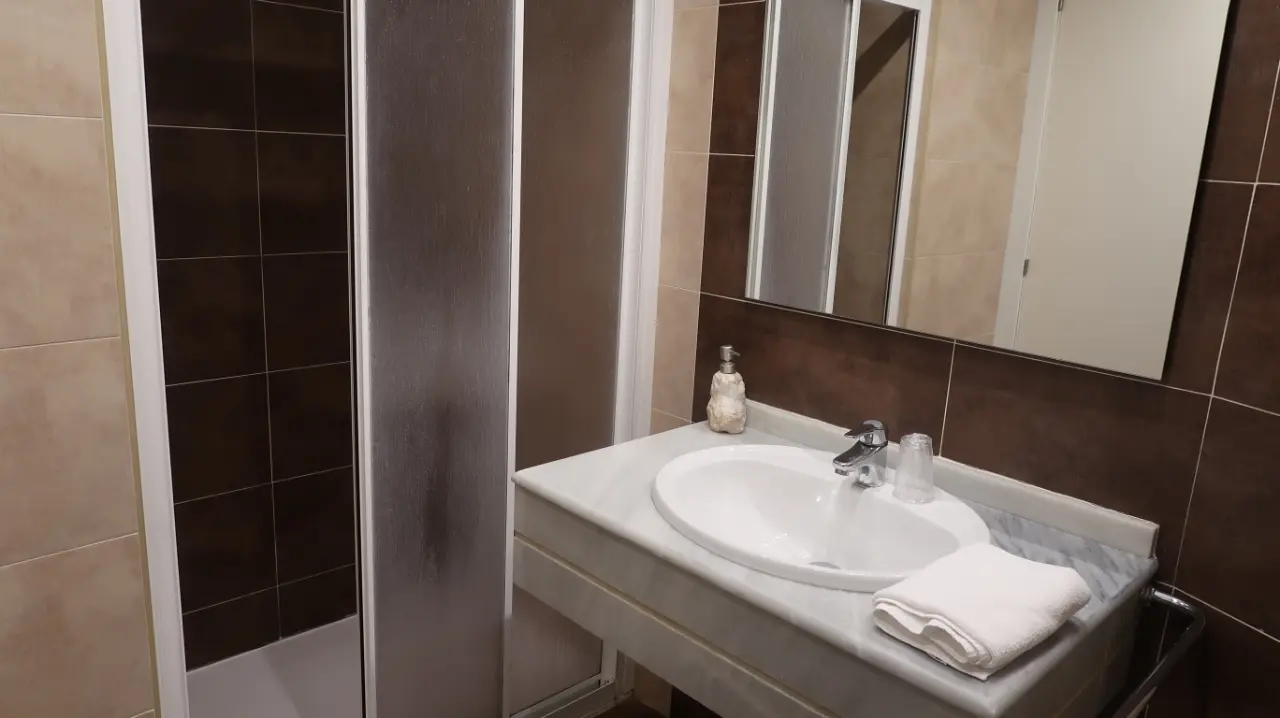 Baño de la Junior Suite con lavabo de encimera blanca, grifo cromado, espejo grande, toalla blanca doblada y mampara