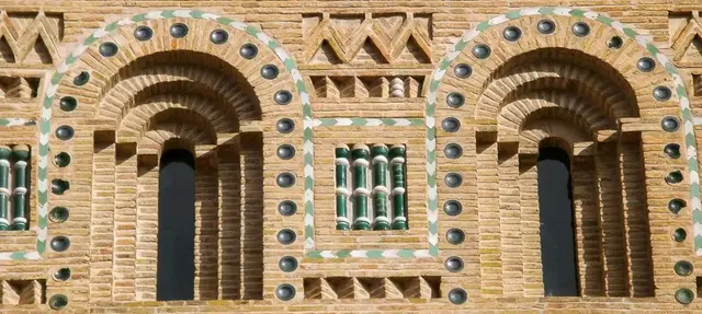 Fachada de ladrillo con arcos decorativos, cerámica verde y blanca, y ventanas enrejadas.